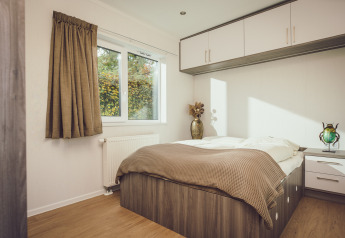 Bright bedroom in a tiny house with double bed, built-in storage, and a large window showing greenery outside.