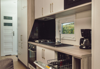 Cucina moderna in una tiny house con lavastoviglie aperta, forno, microonde e macchina del caffè.