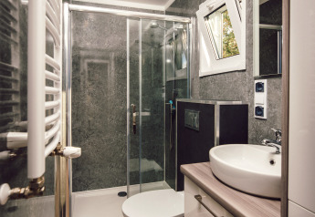 Salle de bain moderne et compacte dans une tiny house avec douche, lavabo, toilettes et sol aspect bois.