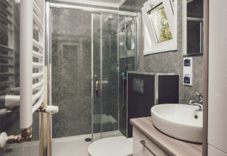 Bagno moderno e compatto in una tiny house, con doccia, lavandino, wc e pavimento effetto legno.