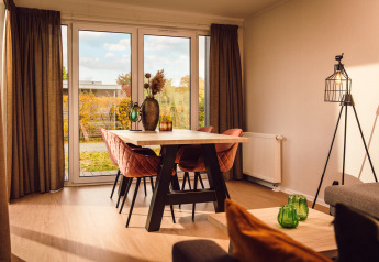 Lys stue med spisebord, lyserøde stole og store vinduer i Tiny cabin på Vakantiepark Hölte, Holland.