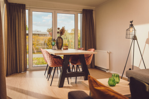 Lichte leefruimte met eettafel, roze stoelen en grote ramen in Tiny Cabin op Vakantiepark Hölte, Nederland.