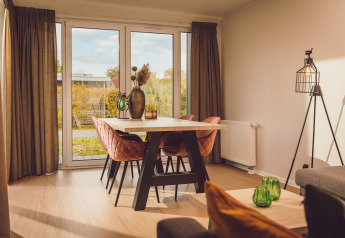 Lichte leefruimte met eettafel, roze stoelen en grote ramen in Tiny Cabin op Vakantiepark Hölte, Nederland.
