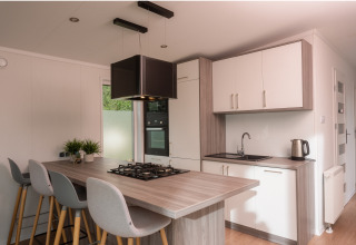 Moderne compacte keuken in een tiny cabin op Vakantiepark Hölte, Nederland, met kookeiland en stoelen.