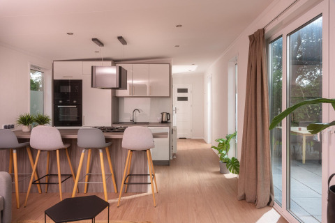 Modernes Tiny House mit heller Küche, Barhockern, Holzfußboden und Blick auf die Terrasse in den Niederlanden.