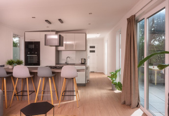 Moderne tiny house keuken met barkrukken, houten vloer en grote ramen, zicht op terras in Nederland.