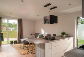 Interior moderno de tiny house con cocina abierta, sala de estar, grandes ventanas y vista al campo verde.