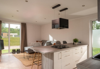 Modern tiny house interior with open kitchen, living area, large windows, and view of green landscape.