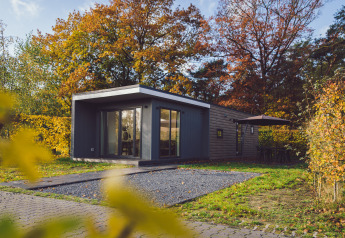 Tiny house moderna Tiny Cabin con vasca idromassaggio, circondata da alberi autunnali a Vakantiepark Hölte, Paesi Bassi.