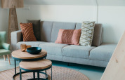Modern living room with grey sofa, decorative cushions and round tables in Big lodge, Holiday park De Boshoek, Netherlands.
