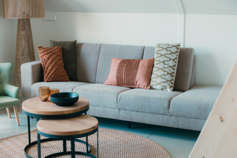 Modern living room with grey sofa, decorative cushions and round tables in Big lodge, Holiday park De Boshoek, Netherlands.