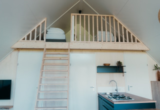 Interior of Big Lodge at Holiday park De Boshoek in the Netherlands with loft beds, kitchen, and ladder.