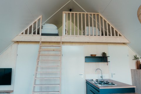 Intérieur du Big lodge au Holiday park De Boshoek aux Pays-Bas avec mezzanine, lits, cuisine et échelle.