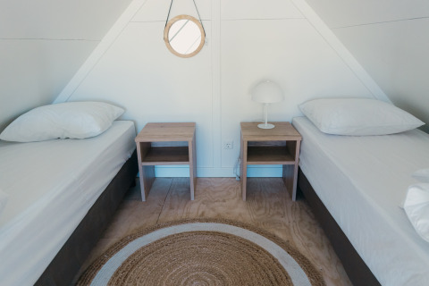 To enkelt senge i et lyst værelse med natborde og lampe på Big lodge i Holiday park De Boshoek, Holland.