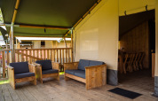 Hyggeligt opholdsområde med træmøbler og overdækning i safari telt ved Camping de Chênefleur, Belgien.