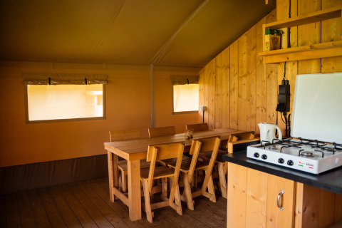 Intérieur d’une tente safari avec meubles en bois, table à manger, chaises et gazinière au Camping de Chênefleur, Belgique.