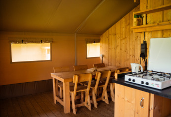 Intérieur d’une tente safari avec meubles en bois, table à manger, chaises et gazinière au Camping de Chênefleur, Belgique.