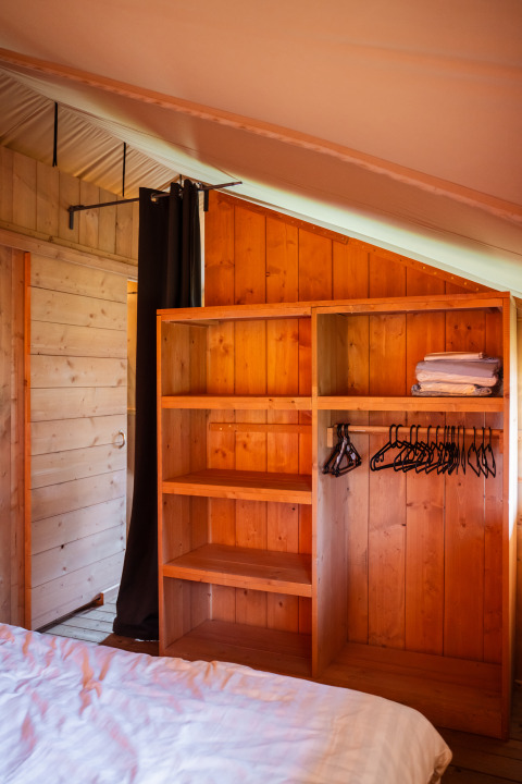 Interior of Safari tent at Camping de Chênefleur, showing wardrobe, shelves, hangers, and towels.