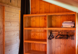 Indvendigt billede af Safari-telt med trægarderobe, bøjlestang, hylder og foldede håndklæder.