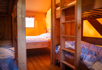 Interieur van een safaritent met stapelbedden en houten meubels bij Camping de Chênefleur in België.