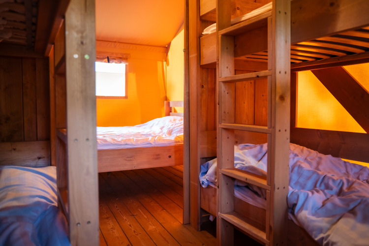 Vista interior de una tienda safari con literas y muebles de madera en Camping de Chênefleur, Bélgica.