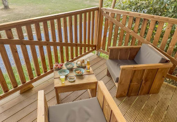Holzterrasse mit zwei Sesseln und Tisch mit Snacks im Safarizelt auf Camping de Chênefleur, Belgien.