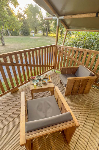 Wooden deck with two chairs and a table with snacks at a safari tent at Camping de Chênefleur, Belgium.