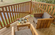 Terraza de madera con dos sillones y mesa con aperitivos en tienda safari en Camping de Chênefleur, Bélgica.