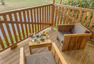 Terraza de madera con dos sillones y mesa con aperitivos en tienda safari en Camping de Chênefleur, Bélgica.