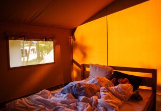 Dos personas duermen en una cómoda cama dentro de una tienda safari en Camping de Chênefleur en Bélgica.