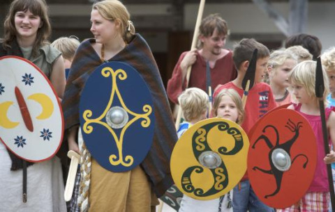 Niños y adultos con disfraces históricos y escudos coloridos en el parque Archeon, Holanda Meridional.