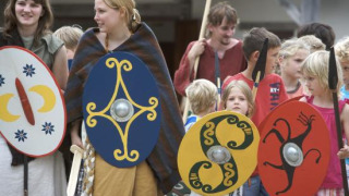 Niños y adultos con disfraces históricos y escudos coloridos en el parque Archeon, Holanda Meridional.