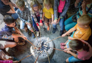 Kinder und Erwachsene rösten Essen über einem Lagerfeuer im Ferienpark Expedition Archeon, Südholland.