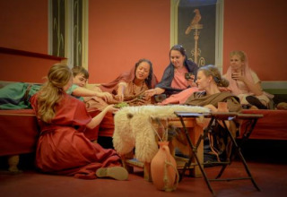 Gruppe mennesker i historisk tøj nyder et måltid i Archeon, en feriepark i Sydholland, Holland.