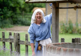 Kvinde i middelaldertøj smiler ved en brønd i Expedition Archeon, et feriepark i Sydholland, Nederlandene.