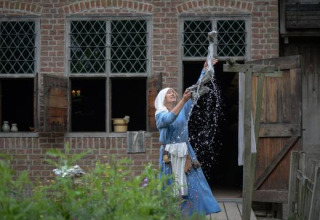 Kvinde i historisk tøj hænger vasketøj op ved en gammel bygning i Expedition Archeon, Syd-Holland, Nederlandene.