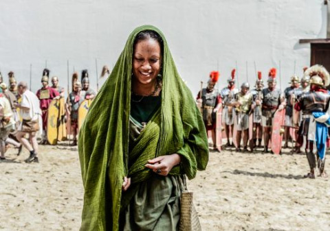 Mujer con túnica verde frente a soldados romanos en Expedition Archeon, parque en Holanda Meridional, Países Bajos.
