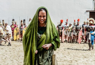 Kvinde i grøn klædedragt foran en gruppe romerske soldater ved Expedition Archeon i Sydholland, Holland.
