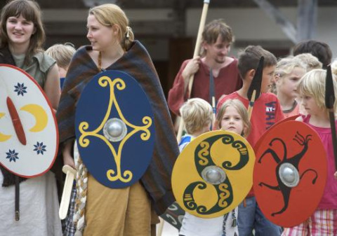 Personas con trajes históricos y escudos coloridos en Expedition Archeon, un parque vacacional en Holanda del Sur.