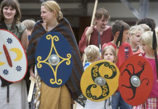 Folk i historiske dragter med farverige skjolde ved Expedition Archeon, en feriepark i Sydholland, Nederlandene.