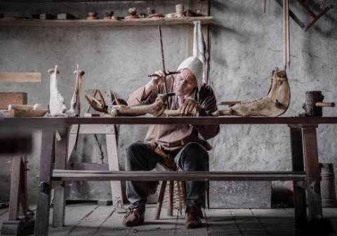 Artesano con ropa histórica trabaja con huesos en una mesa de madera en Expedition Archeon, Holanda Meridional.
