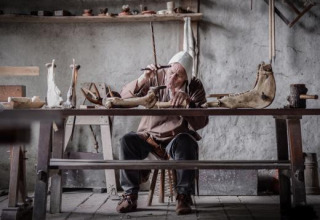 Ambachtsman in historische kledij werkt met beenderen aan een houten tafel in Expedition Archeon, Zuid-Holland.