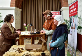 Personer iklædt historiske kostumer samtaler ved en bod på Expedition Archeon, en park i Sydholland.