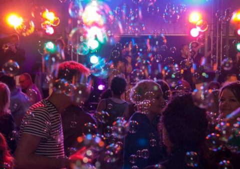 Personas bailando entre burbujas y luces de colores en Expedition Archeon, un parque vacacional en Holanda Sur.