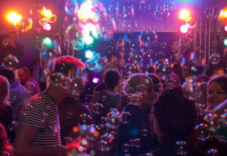Personas bailando entre burbujas y luces de colores en Expedition Archeon, un parque vacacional en Holanda Sur.