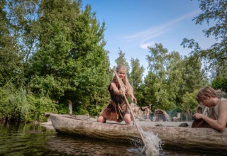 Personer i stammebeklædning sejler i en udhugget træbåd på en sø i Archeon, Holland.