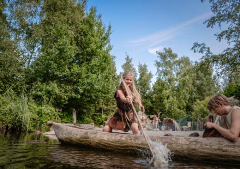 Personas con ropa tribal reman en una canoa tallada en el parque Archeon, Holanda Meridional, Países Bajos.