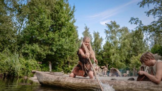 Personas con ropa tribal reman en una canoa tallada en el parque Archeon, Holanda Meridional, Países Bajos.