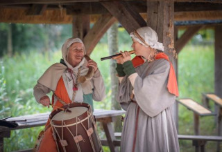 To mennesker i middelaldertøj spiller tromme og fløjte i et historisk omgivelser ved Expedition Archeon.