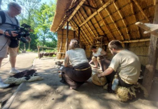 Fotograf optager personer i middelaldertøj, der arbejder ved et stråtækt hus i ferieparken Expedition Archeon.